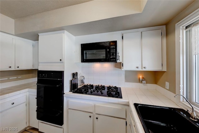 kitchen with tile countertops, a sink, black appliances, white cabinets, and a warming drawer