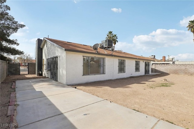 rear view of property with a gate, stucco siding, central AC, and fence