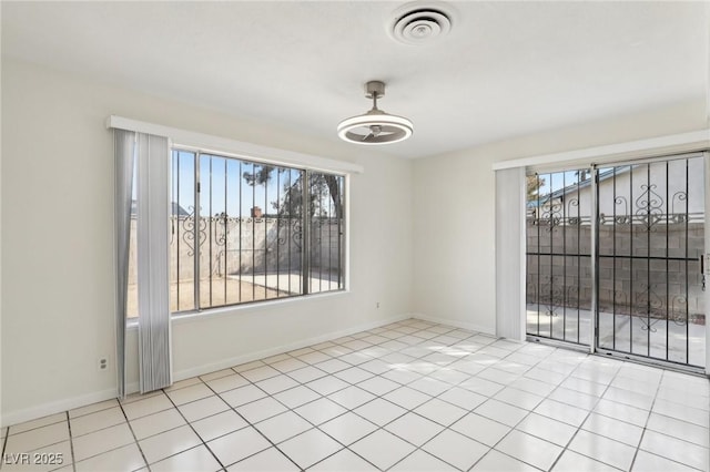 empty room featuring tile patterned floors, visible vents, a healthy amount of sunlight, and baseboards