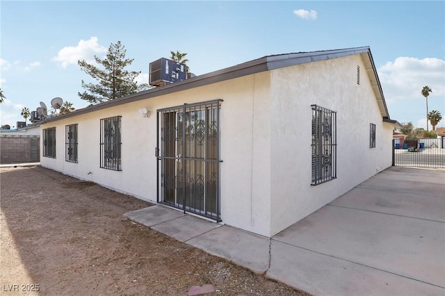 rear view of house with stucco siding, cooling unit, and fence