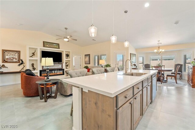 kitchen with stainless steel dishwasher, vaulted ceiling, a sink, an island with sink, and decorative light fixtures