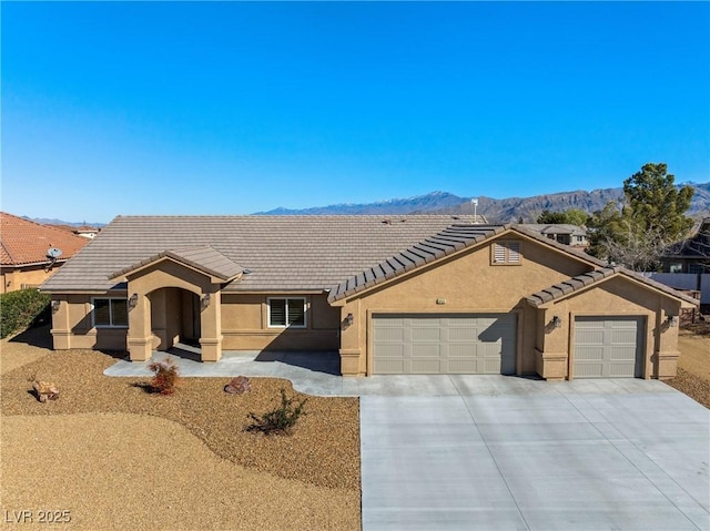 ranch-style home with a tile roof, a mountain view, a garage, and stucco siding