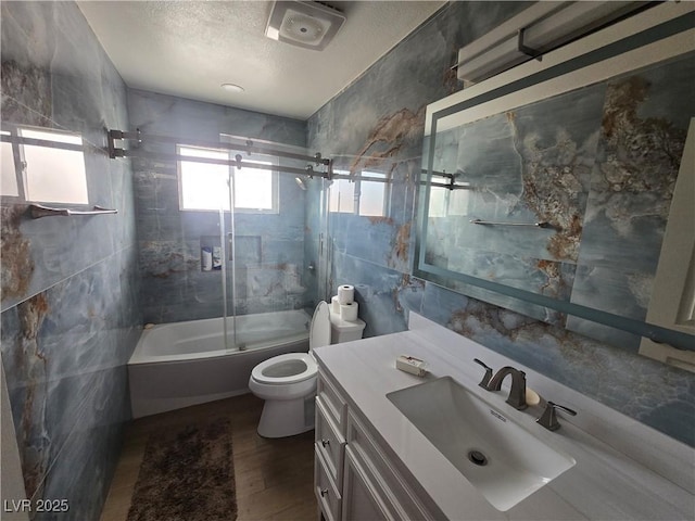 bathroom with toilet, a textured ceiling, wood finished floors, tile walls, and vanity