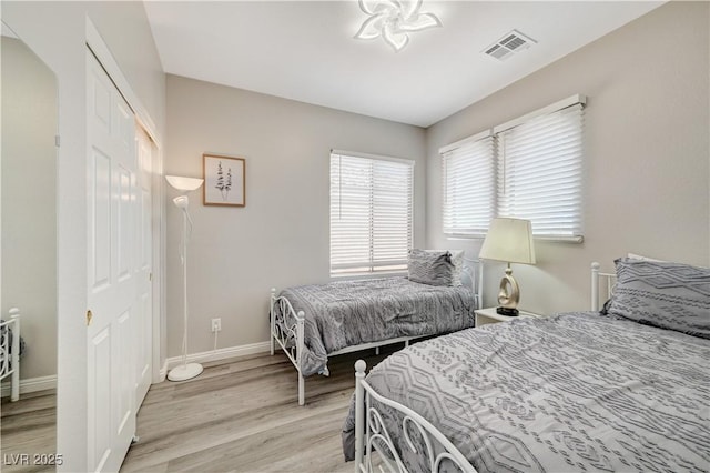 bedroom featuring light wood-type flooring, visible vents, a closet, arched walkways, and baseboards