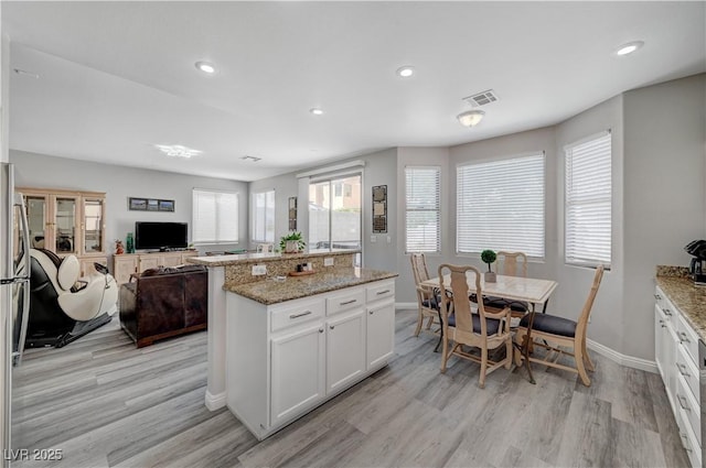 kitchen with light wood finished floors, a center island, open floor plan, recessed lighting, and white cabinetry