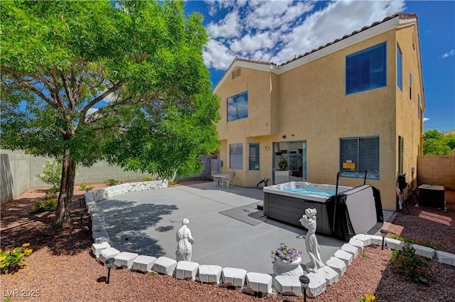 rear view of property featuring stucco siding, a hot tub, a fenced backyard, cooling unit, and a patio area