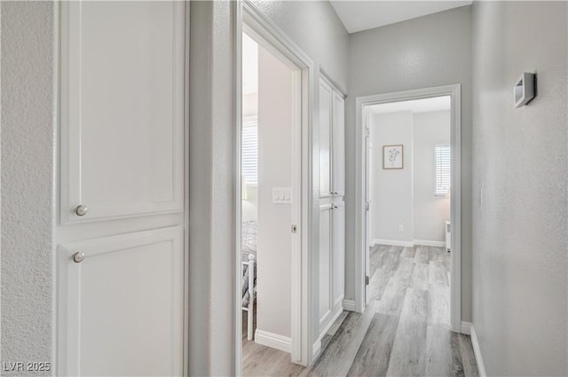 corridor with light wood-style flooring and baseboards