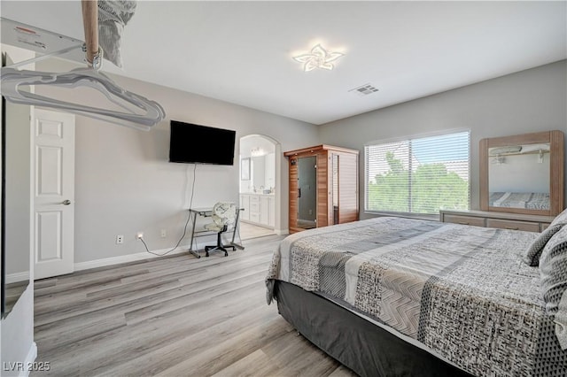 bedroom with visible vents, baseboards, wood finished floors, arched walkways, and ensuite bath