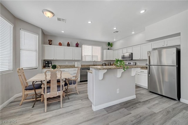 kitchen with visible vents, a kitchen island, white cabinets, appliances with stainless steel finishes, and a kitchen bar