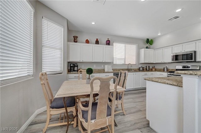 kitchen with visible vents, light wood-style flooring, white cabinets, stainless steel appliances, and a sink