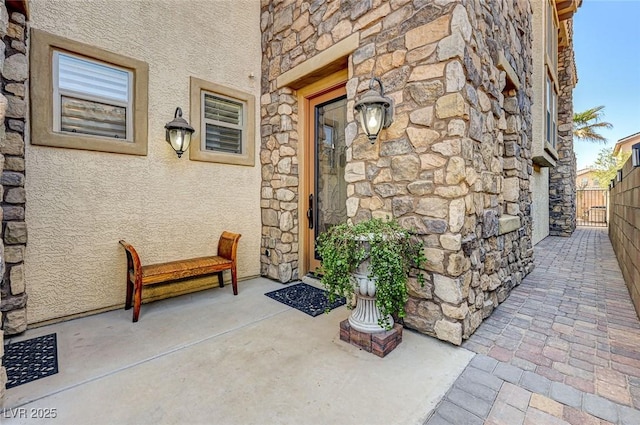 entrance to property featuring stucco siding, stone siding, and fence