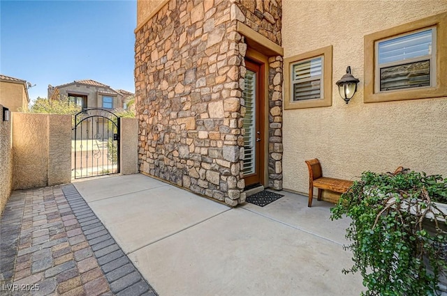 entrance to property with stone siding, stucco siding, fence, and a gate