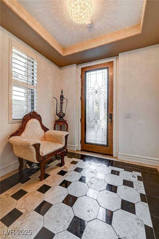 entrance foyer with a notable chandelier, a textured ceiling, a raised ceiling, and baseboards