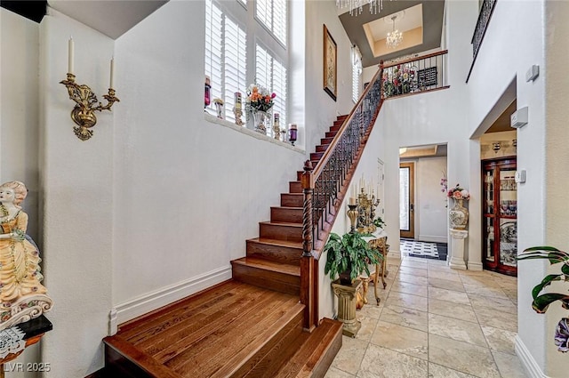 foyer entrance featuring baseboards, an inviting chandelier, a towering ceiling, and stairs