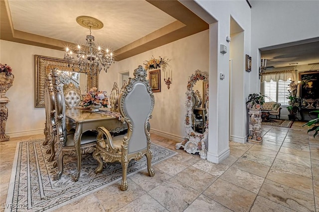 dining space featuring a raised ceiling, a notable chandelier, and baseboards