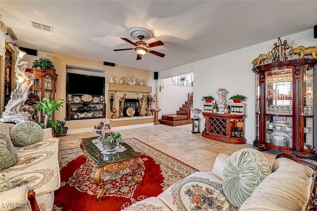 living area with stairway, a fireplace with raised hearth, visible vents, and ceiling fan