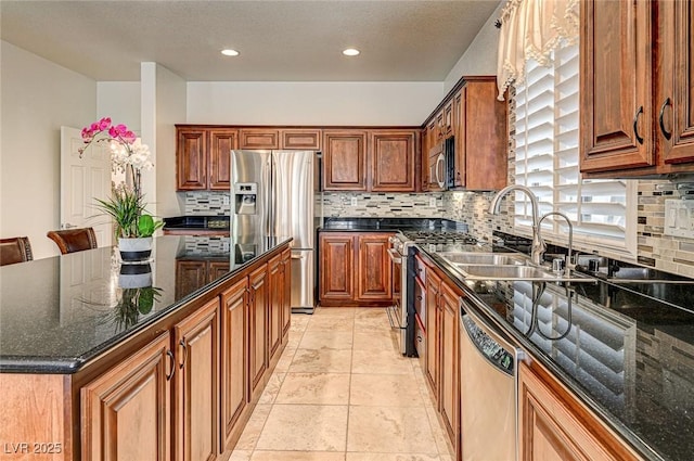 kitchen with dark stone counters, a sink, appliances with stainless steel finishes, tasteful backsplash, and a center island