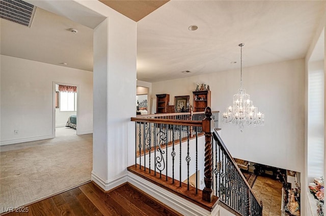 stairway featuring wood finished floors, visible vents, baseboards, an inviting chandelier, and carpet flooring