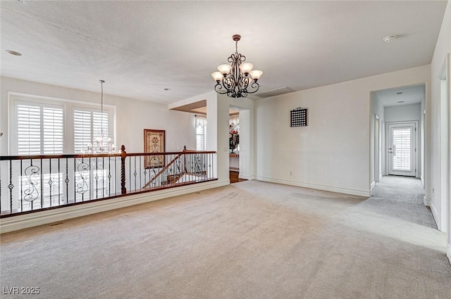 spare room featuring a notable chandelier, carpet, and baseboards