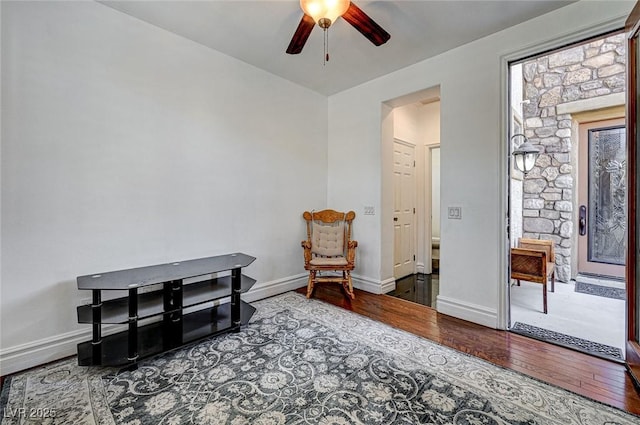 living area featuring baseboards, wood-type flooring, and ceiling fan