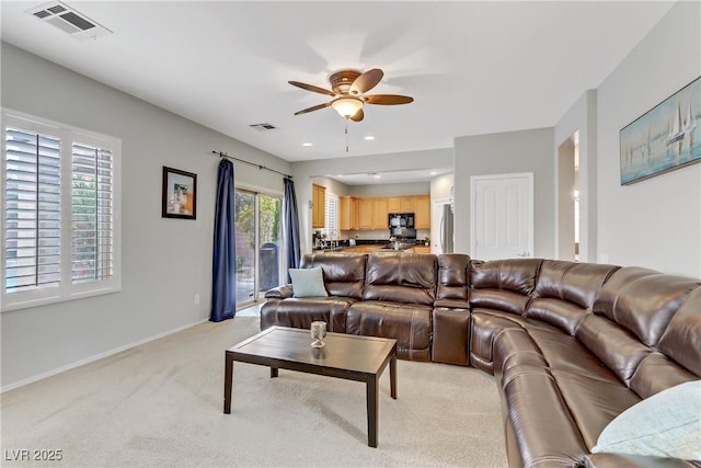 living area with light carpet, visible vents, baseboards, and a ceiling fan