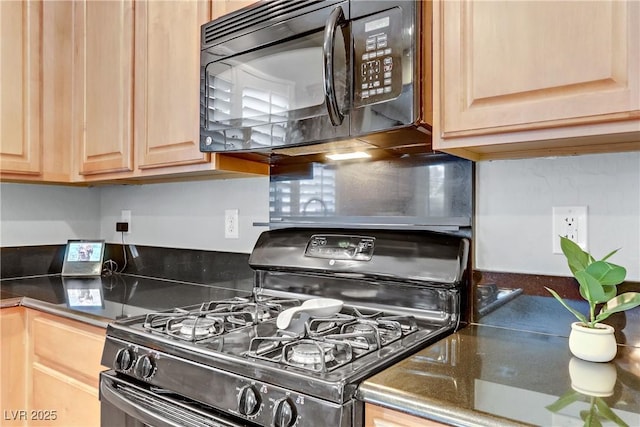 kitchen with light brown cabinets, gas stove, dark countertops, and black microwave