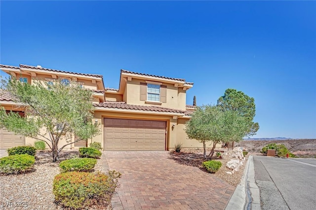 mediterranean / spanish house featuring a tiled roof, decorative driveway, a garage, and stucco siding