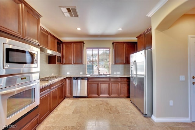 kitchen with visible vents, under cabinet range hood, light stone counters, stainless steel appliances, and a sink