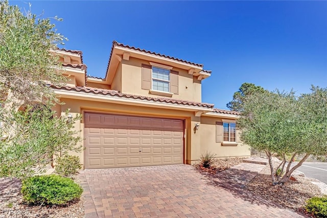 mediterranean / spanish house featuring a tiled roof, decorative driveway, an attached garage, and stucco siding