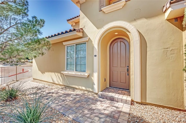 property entrance featuring stucco siding, a tile roof, and fence