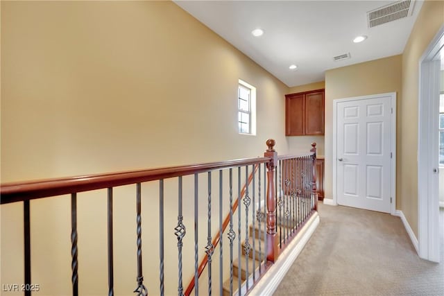 hall with an upstairs landing, visible vents, light carpet, and baseboards