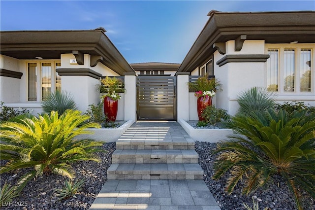 doorway to property featuring stucco siding and a gate