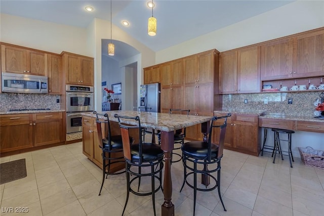 kitchen featuring a kitchen breakfast bar, appliances with stainless steel finishes, light tile patterned flooring, and brown cabinetry