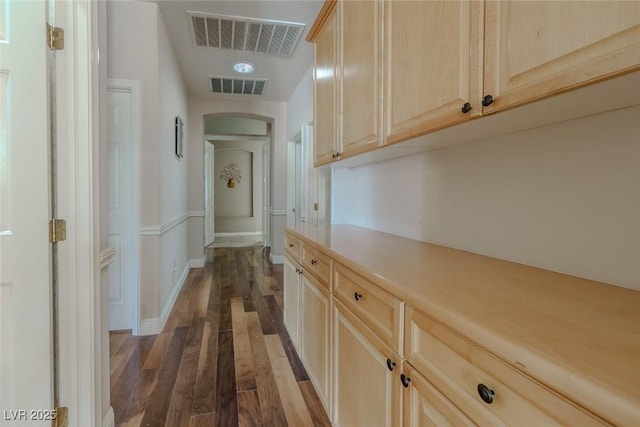 hallway featuring arched walkways, visible vents, baseboards, and dark wood-style floors