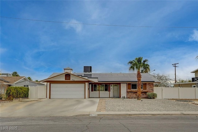 ranch-style home featuring driveway, fence, an attached garage, brick siding, and solar panels