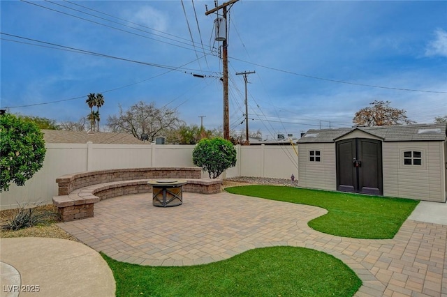 view of patio with an outbuilding, a storage unit, a fenced backyard, and an outdoor fire pit