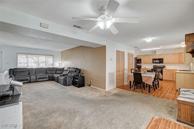 living area featuring visible vents, light carpet, a textured ceiling, and ceiling fan