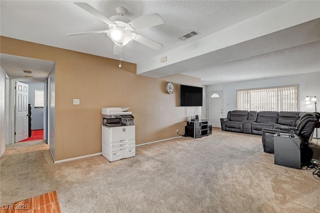 carpeted living area featuring baseboards, visible vents, a textured ceiling, and a ceiling fan