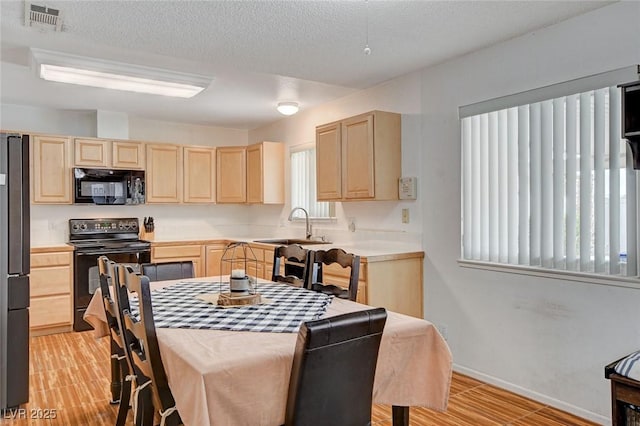 kitchen with visible vents, black appliances, light brown cabinetry, a sink, and light countertops