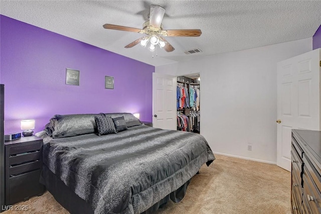 bedroom with visible vents, a walk in closet, ceiling fan, light colored carpet, and a textured ceiling