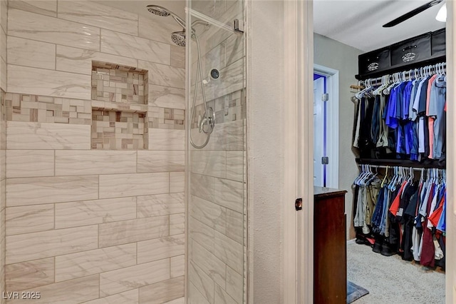 full bath featuring vanity, tiled shower, a walk in closet, and a ceiling fan