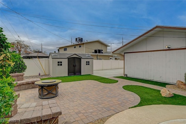 view of patio featuring a storage shed, a fenced backyard, an outbuilding, and an outdoor fire pit