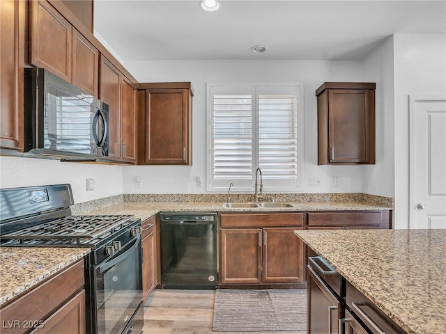 kitchen featuring black appliances, light stone counters, recessed lighting, and a sink