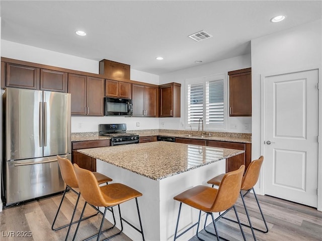 kitchen with a sink, visible vents, black appliances, and a breakfast bar area