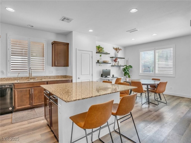 kitchen with visible vents, a breakfast bar, a sink, dishwasher, and light wood-type flooring