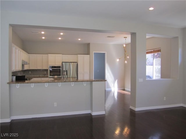 kitchen with baseboards, dark wood finished floors, a peninsula, white cabinets, and appliances with stainless steel finishes