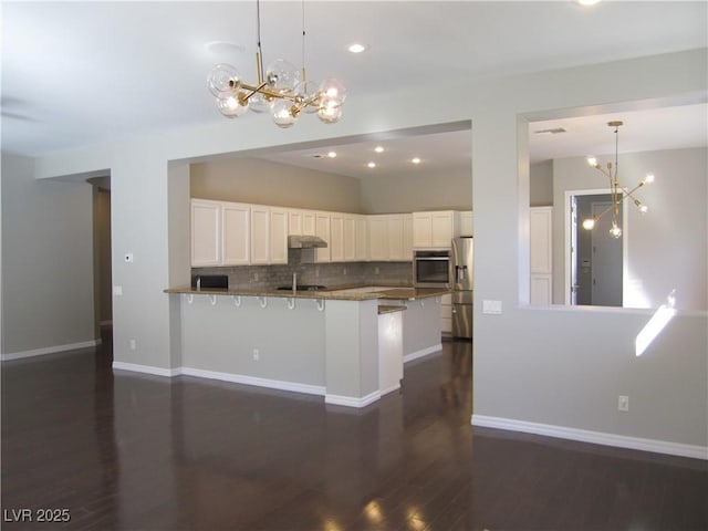 kitchen with an inviting chandelier, a peninsula, decorative backsplash, appliances with stainless steel finishes, and white cabinetry