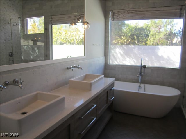 bathroom featuring double vanity, a soaking tub, tile walls, and a sink