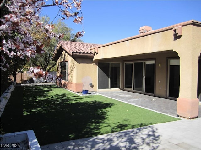 rear view of property with a patio, fence, a yard, stucco siding, and a tiled roof