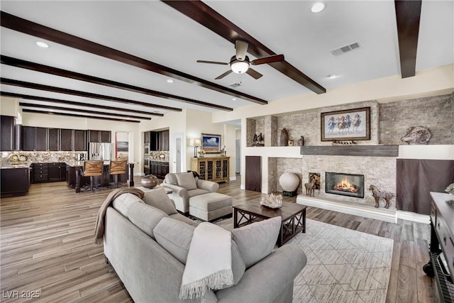 living area with a ceiling fan, visible vents, beam ceiling, a fireplace, and light wood-style floors